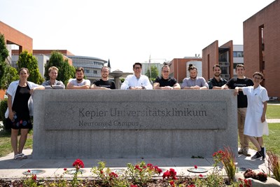 Ein Team aus Forscherinnen und Forschern positioniert sich um das Schild "Kepler Universitätsklinikum - Neuromed Campus"
