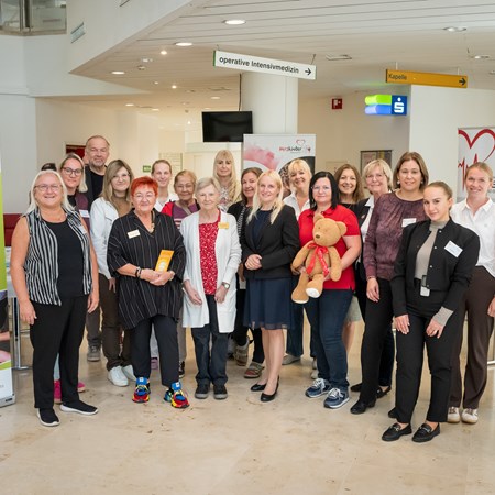 Gruppe von Frauen und ein Mann posieren mit einem Teddybären in einem Krankenhausflur in Österreich.