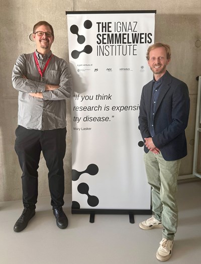 Ignaz Semmelweis Institute: Zwei Männer stehen vor einem Banner mit dem Institutnamen und einem Zitat.