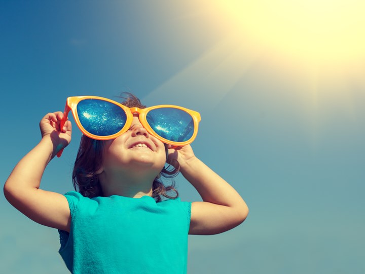 Kind mit übergroßer Sonnenbrille blickt in die Sonne
