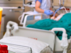 Medikamente auf einem Tisch, dahinter Patientenbett auf Intensivstation mit Pflegekraft