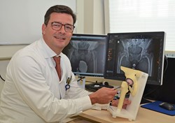 Prof. Gotterbarm zeigt auf künstliches Gelenk mit Röntgen im Hintergrund